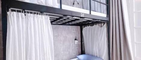 Una cama litera con cortinas blancas, un cajón pequeño y una ventana con cortinas.
