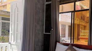 A hotel room with a bed, a window with curtains, and a view of the outside buildings. - Amy Hostel Hue (Hue)