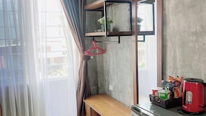 A compact kitchen with a wooden countertop, a refrigerator, a hanging shelf with a plant, and a window with curtains. - Amy Hostel Hue (Hue)