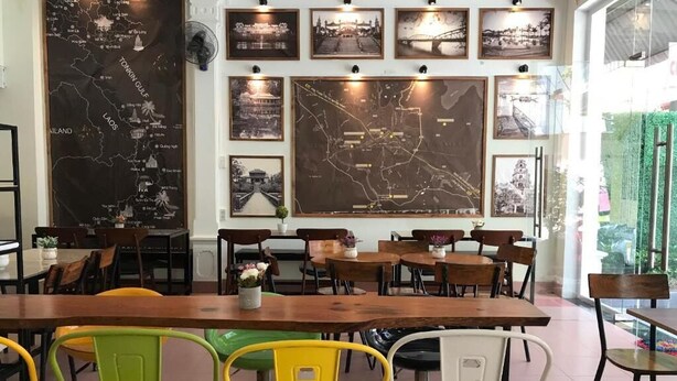 A restaurant with wooden tables and chairs, a large map on the wall, and framed pictures. - Amy Hostel Hue (Hue)
