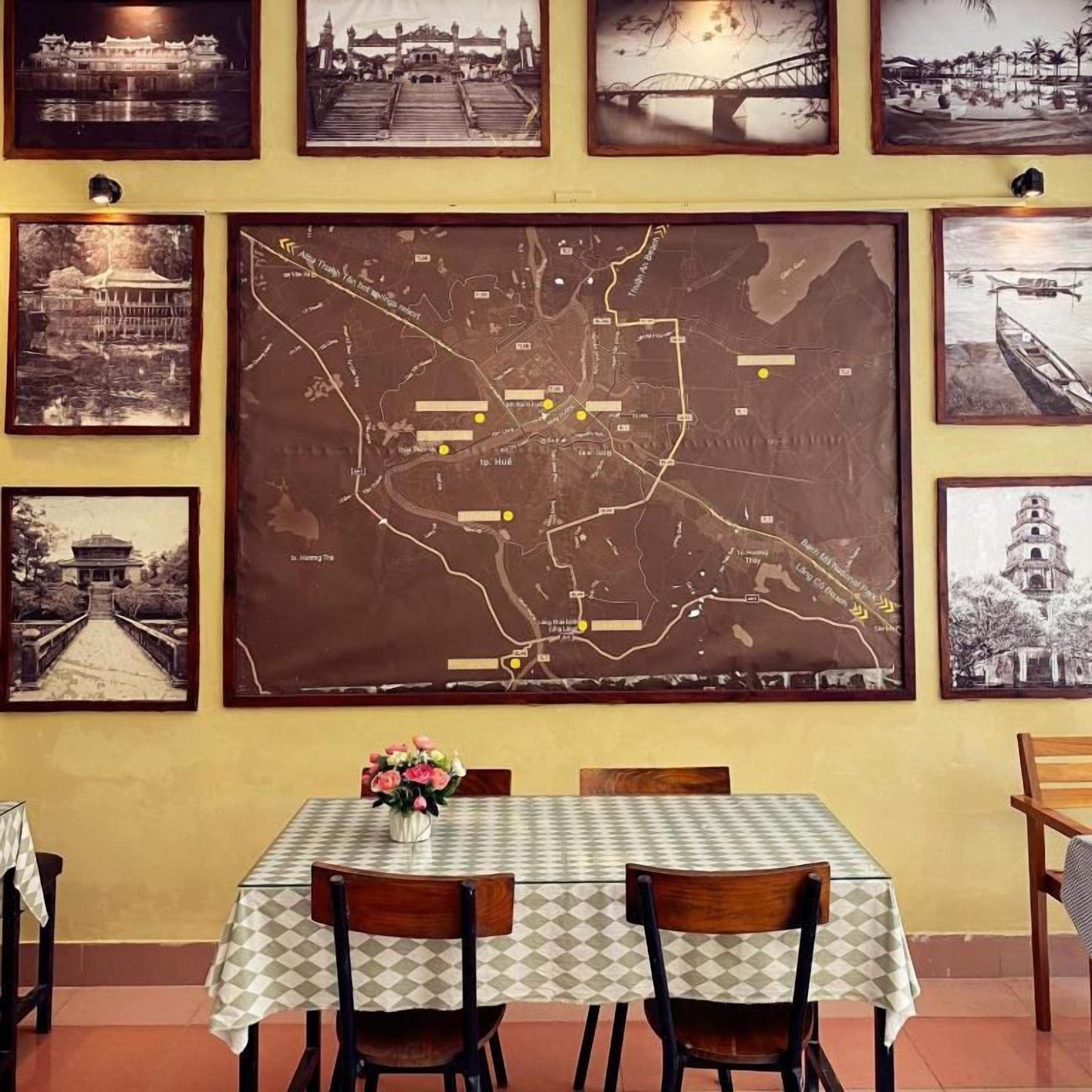 Un comedor con una mesa lista para dos personas, un mapa en la pared y fotografías enmarcadas.