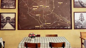 A dining area with a table set for two, a map on the wall, and framed photographs. - Amy Hostel Hue (Hue)