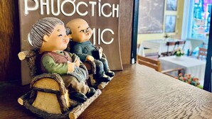 A wooden table with a decorative figurine of two children on a swing. In the background, there's a sign with the text "PHUÓC TIÊN". - Amy Hostel Hue (Hue)