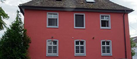 A red building with multiple windows and a sloped roof. There are several parked cars in front.