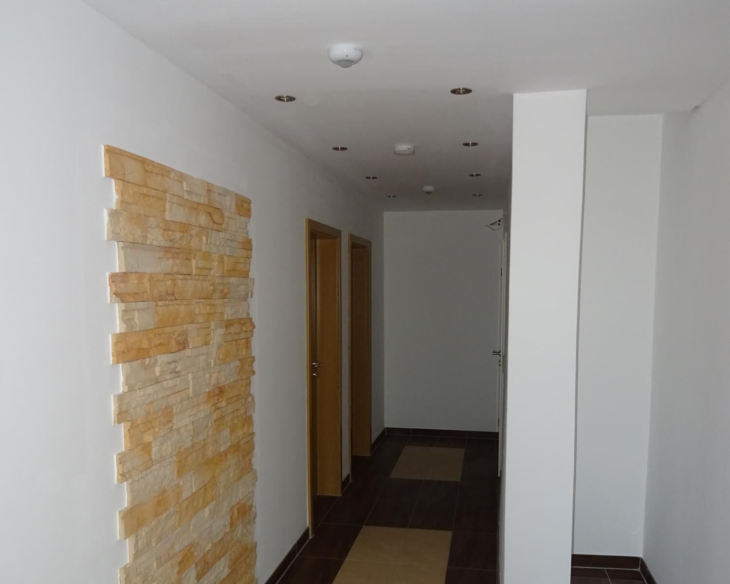 Een gang met een stenen muur, een houten deur en een betegelde vloer.