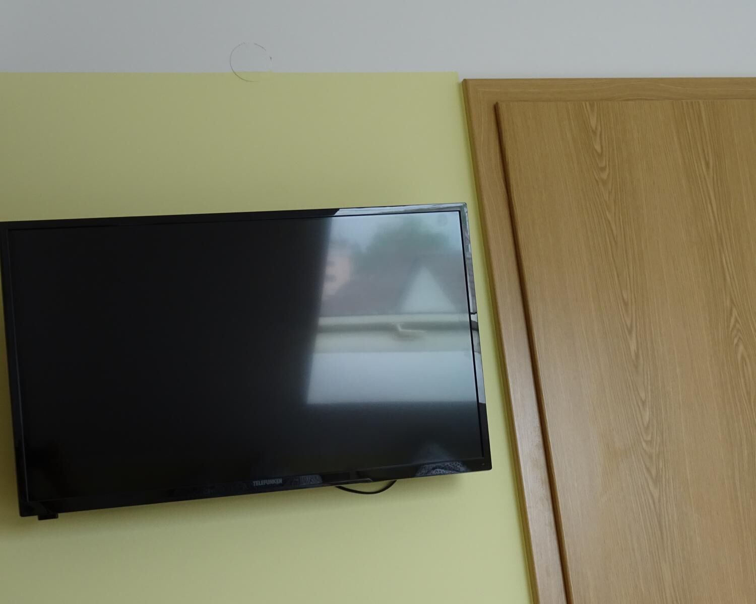 A flat-screen TV mounted on a light yellow wall, next to a wooden door.