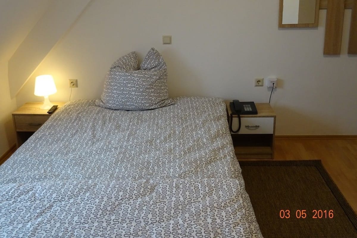 A bedroom with a bed, a bedside lamp, a nightstand, a phone, and a mirror on the wall.