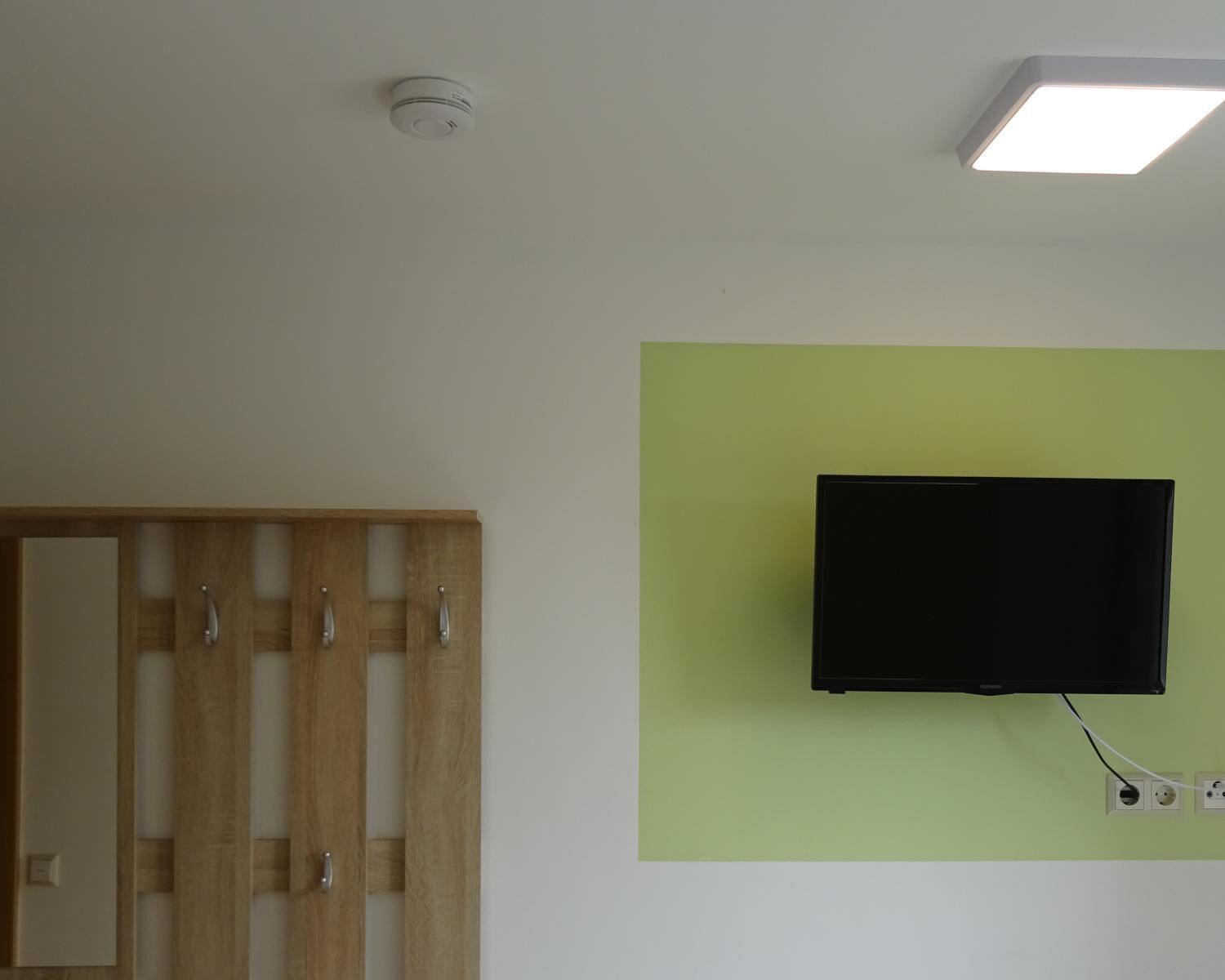 Ein Zimmer mit einem Holzschrank, einem Wandfernseher und einer Deckenleuchte.