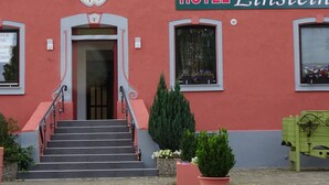 A hotel entrance with a red facade, a staircase leading to the door, and a sign reading "HOTEL Einstein". - Hotel Einstein (Bad Krozingen)