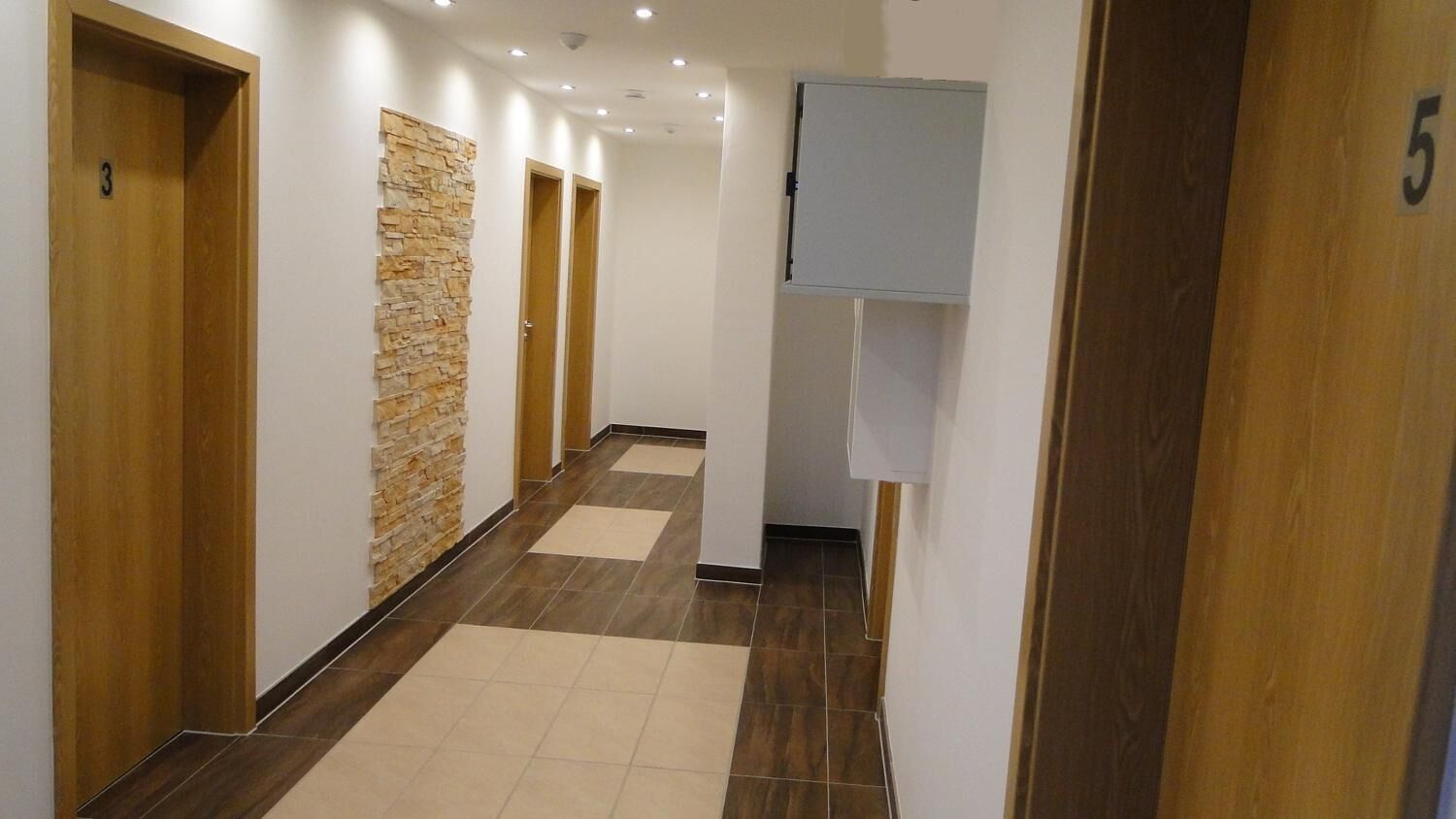 A hallway with wooden doors, a stone accent wall, and a tiled floor.