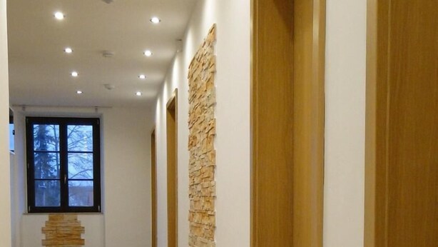 A hallway with wooden doors, a stone accent wall, and a patterned floor. - Hotel Einstein (Bad Krozingen)