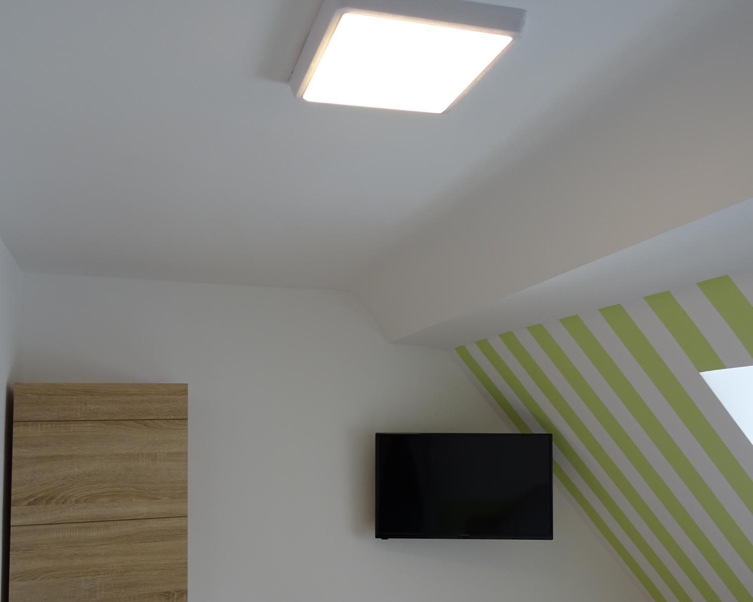 A room with a flat-screen TV mounted on the wall, a wooden cabinet, and a ceiling light fixture.