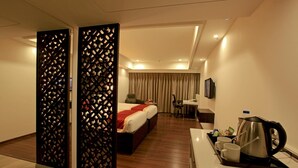 A hotel room with a bed, a desk with a coffee maker, and a TV on the wall. - Goutham Grand Hotel (Tenali)