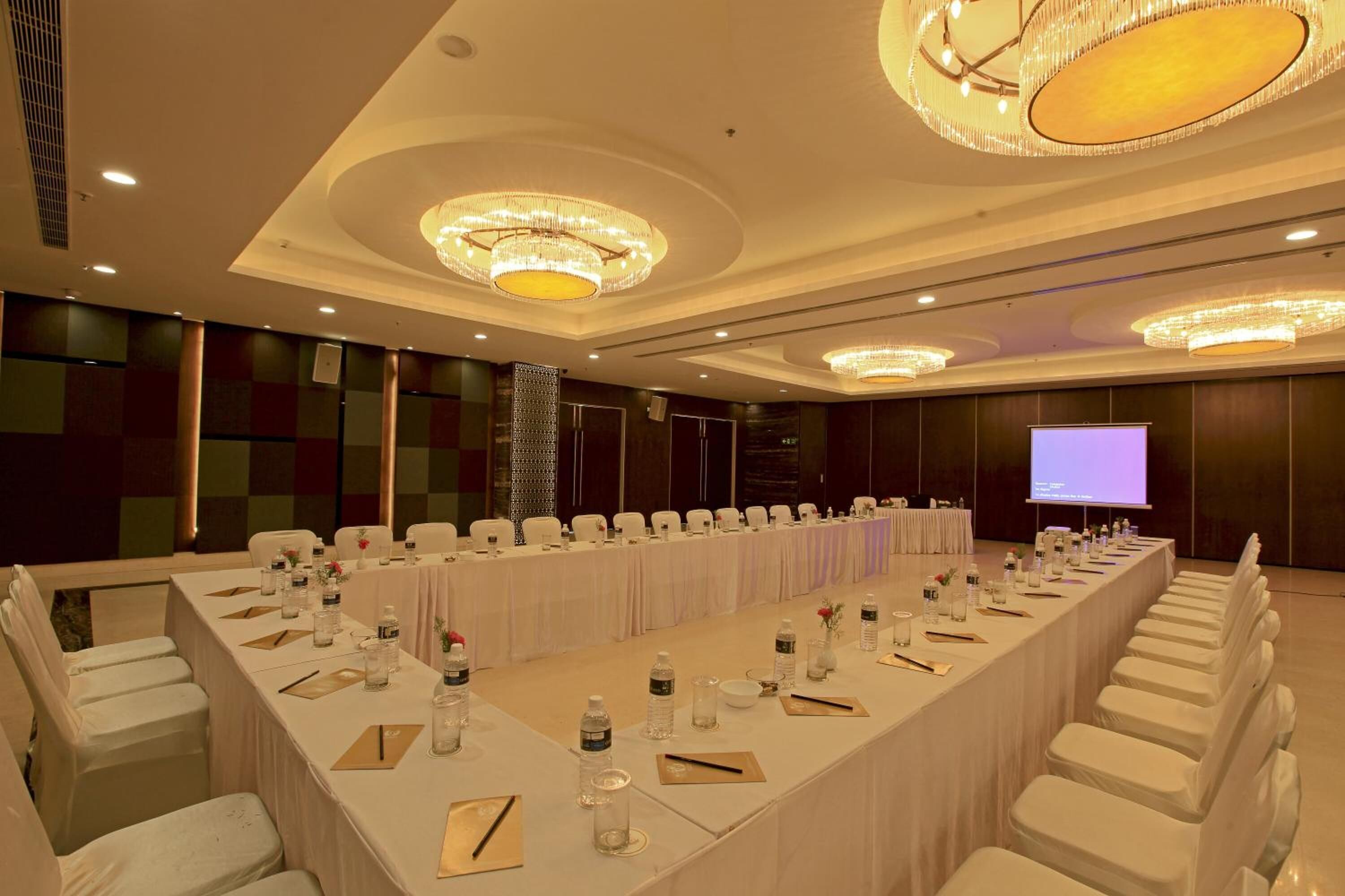 A conference room with a long table, white chairs, and chandeliers.