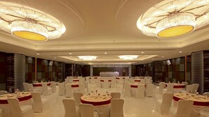 A banquet hall with round tables and white chairs, chandeliers, and a stage in the background. - Goutham Grand Hotel (Tenali)