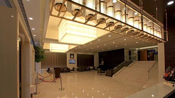 A spacious lobby with a high ceiling, a staircase, and a reception desk. - Goutham Grand Hotel (Tenali)
