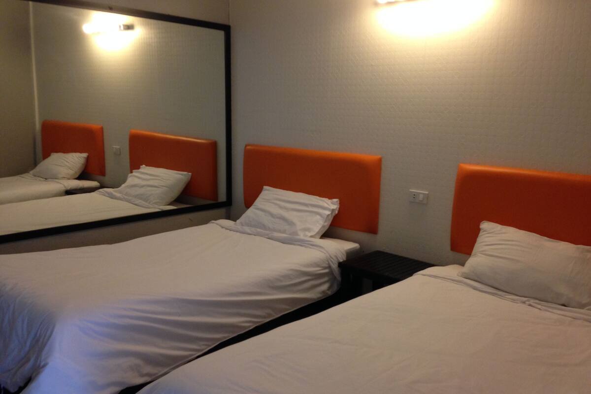 A hotel room with two single beds, each with an orange headboard and white bedding. A large mirror is mounted on the wall above the beds.
