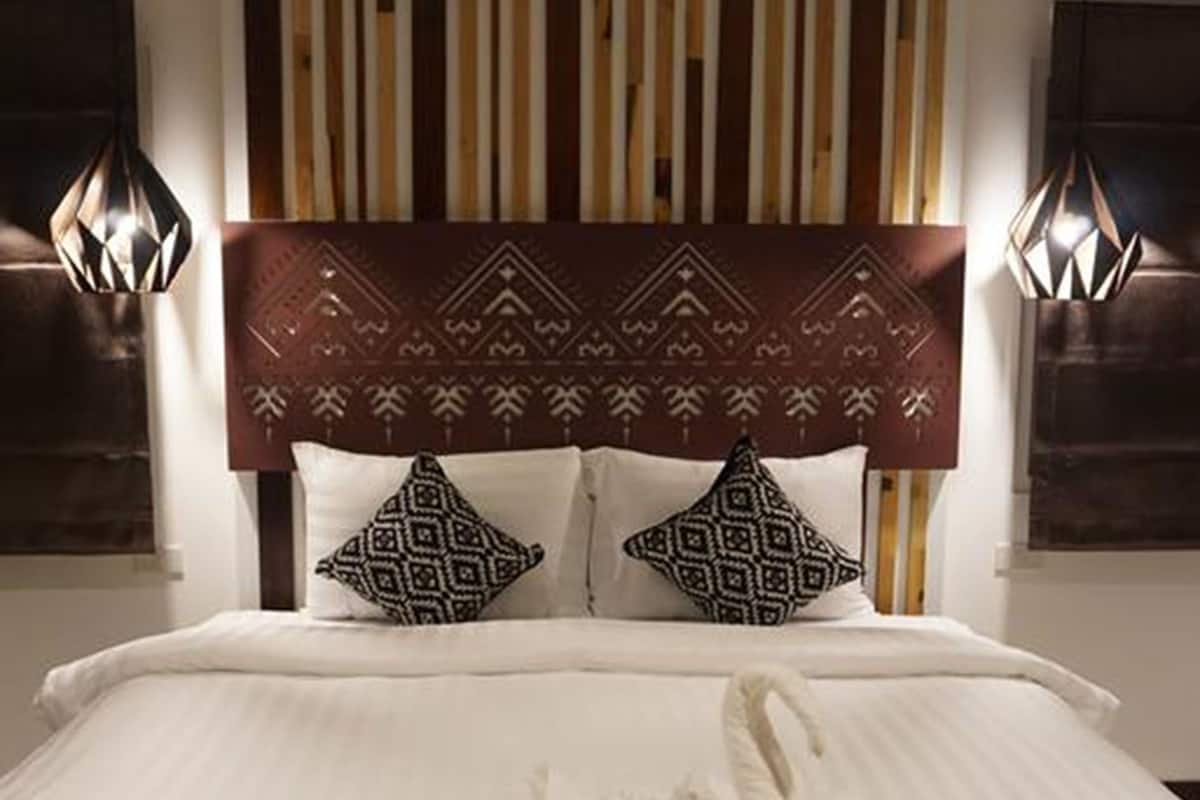 Habitación de hotel con una cama, cabecera con diseño estampado, dos almohadas y un juego de toallas sobre la cama.