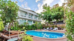 A swimming pool with lounge chairs, surrounded by lush greenery and a multi-story building with balconies. - My Chiang Mai Boutique Lodge (Chiang Mai)