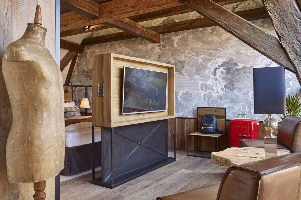 A cozy living room with a fireplace, wooden beams, a mounted TV, and a stone wall.