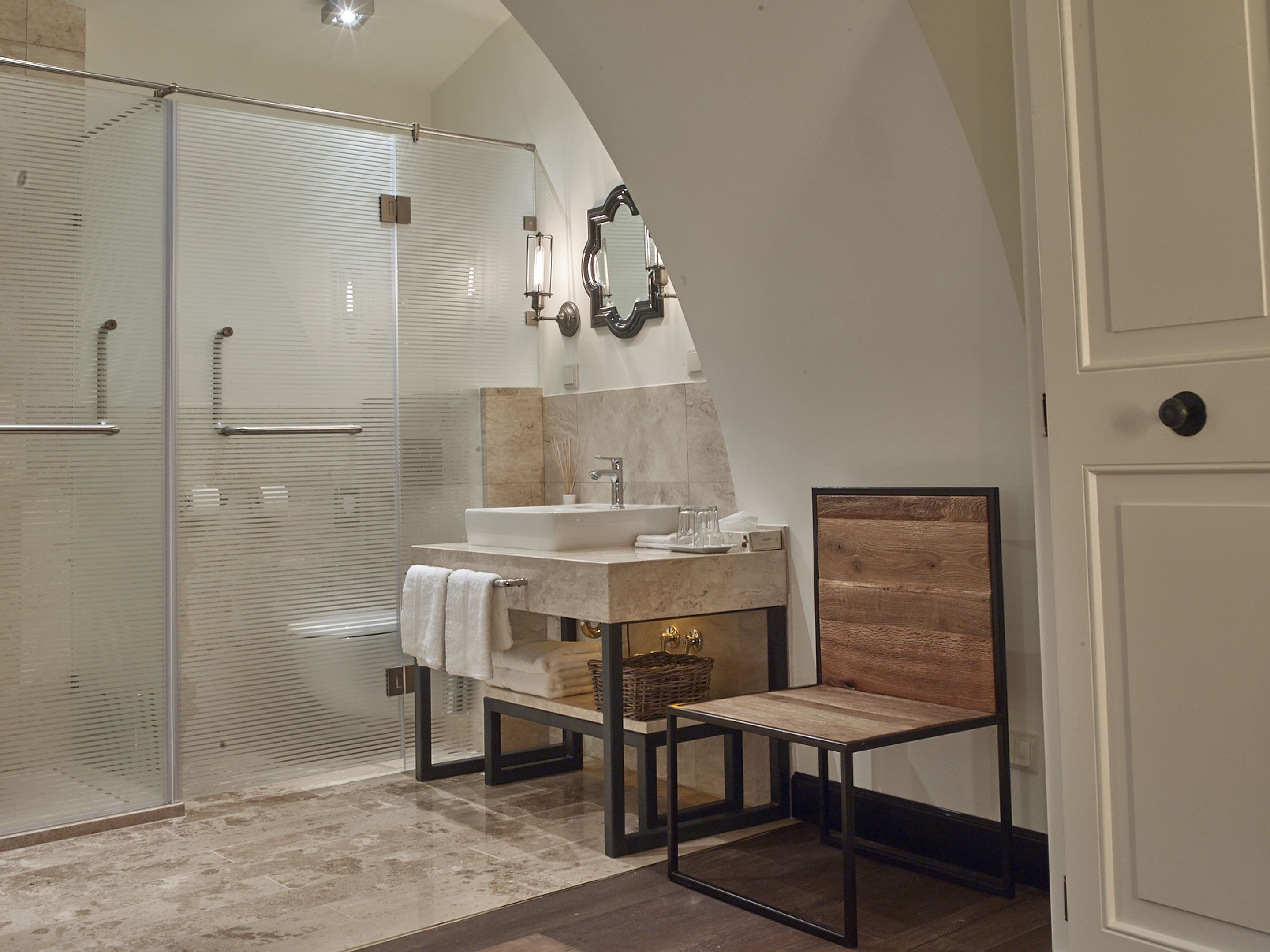 A modern bathroom with a glass shower enclosure, a vanity with a sink and mirror, and a wooden chair.