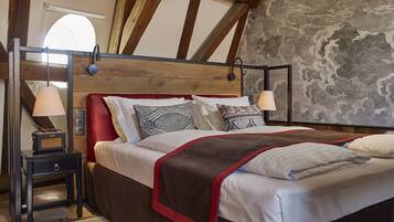 A bedroom with a wooden ceiling, a bed with patterned pillows, a nightstand with a lamp, and a stone wall.
