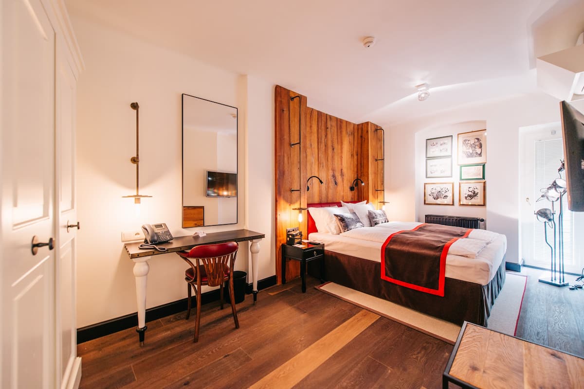A bedroom with a wooden headboard, a desk with a chair, a bed with a red blanket, and framed pictures on the wall.