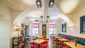 Un restaurante con techos altos en arco, mesas de madera, sillas rojas y una columna central con un reloj.