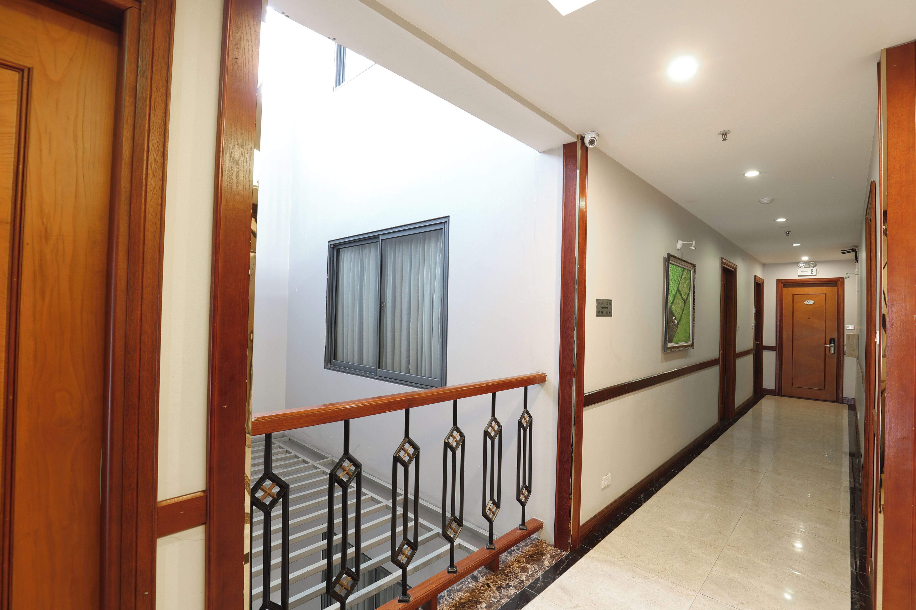 Um corredor de hotel com portas de madeira, uma escada com corrimão de metal e chão revestido de azulejos.