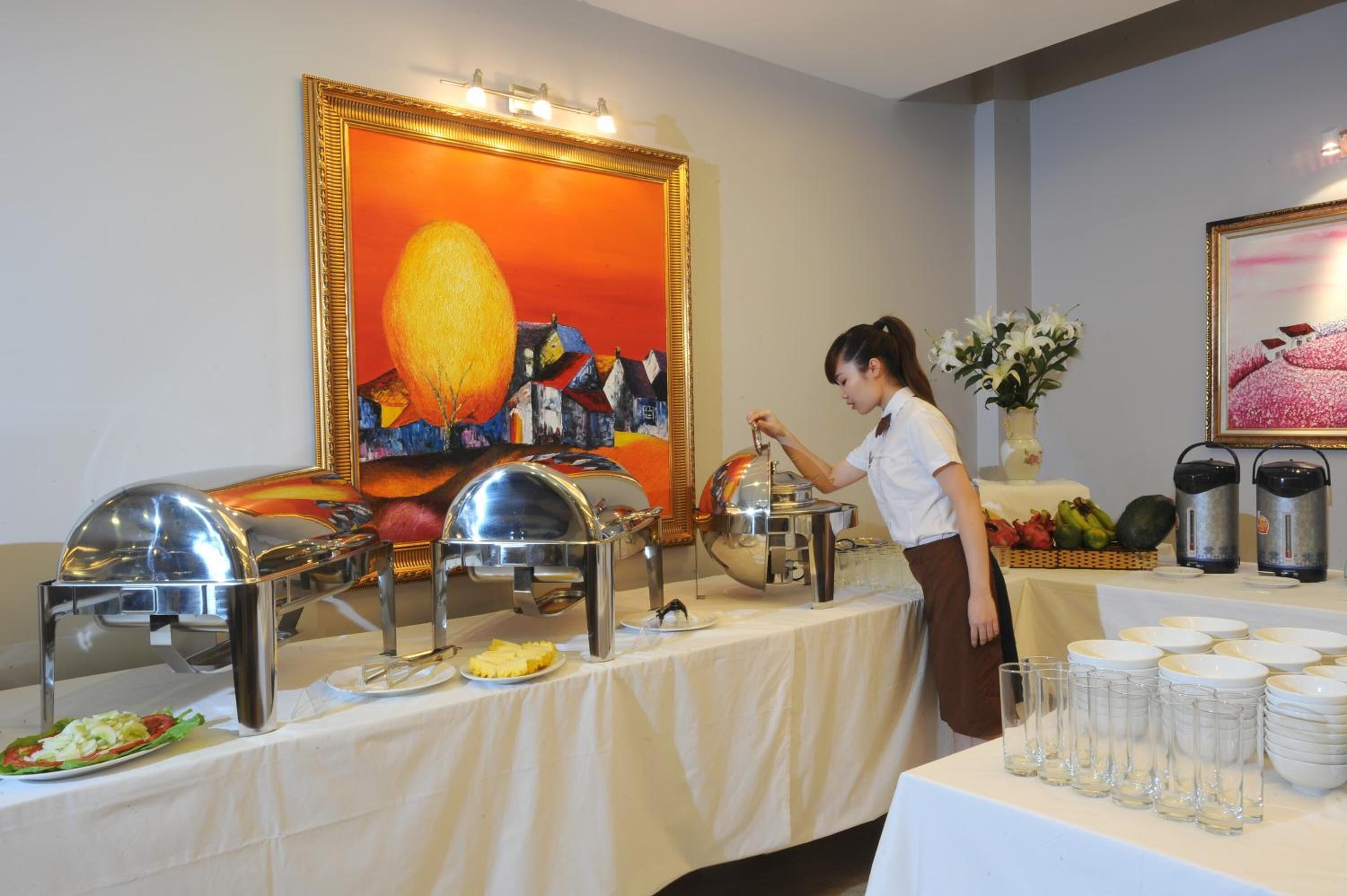 A buffet setup with multiple food stations, a person serving, and decorative paintings on the walls.