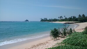 A beach with clear turquoise water, a sandy shore, and a small island in the distance. - Jungleside House (Hikkaduwa)