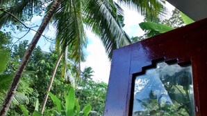 A view through a window with a red frame, looking at a tropical landscape with palm trees and dense foliage. - Jungleside House (Hikkaduwa)