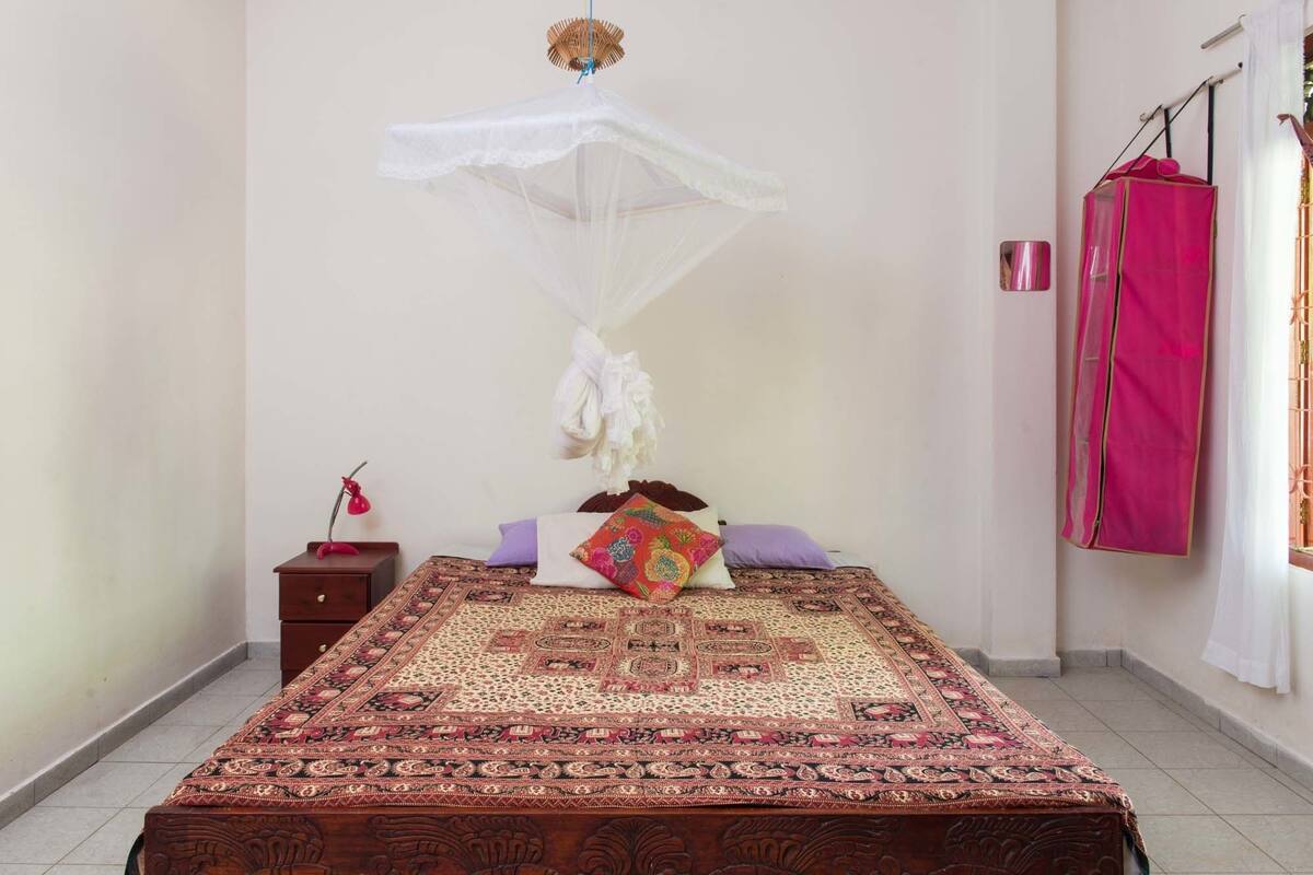 A bedroom with a bed, a nightstand, a lamp, and a mosquito net.