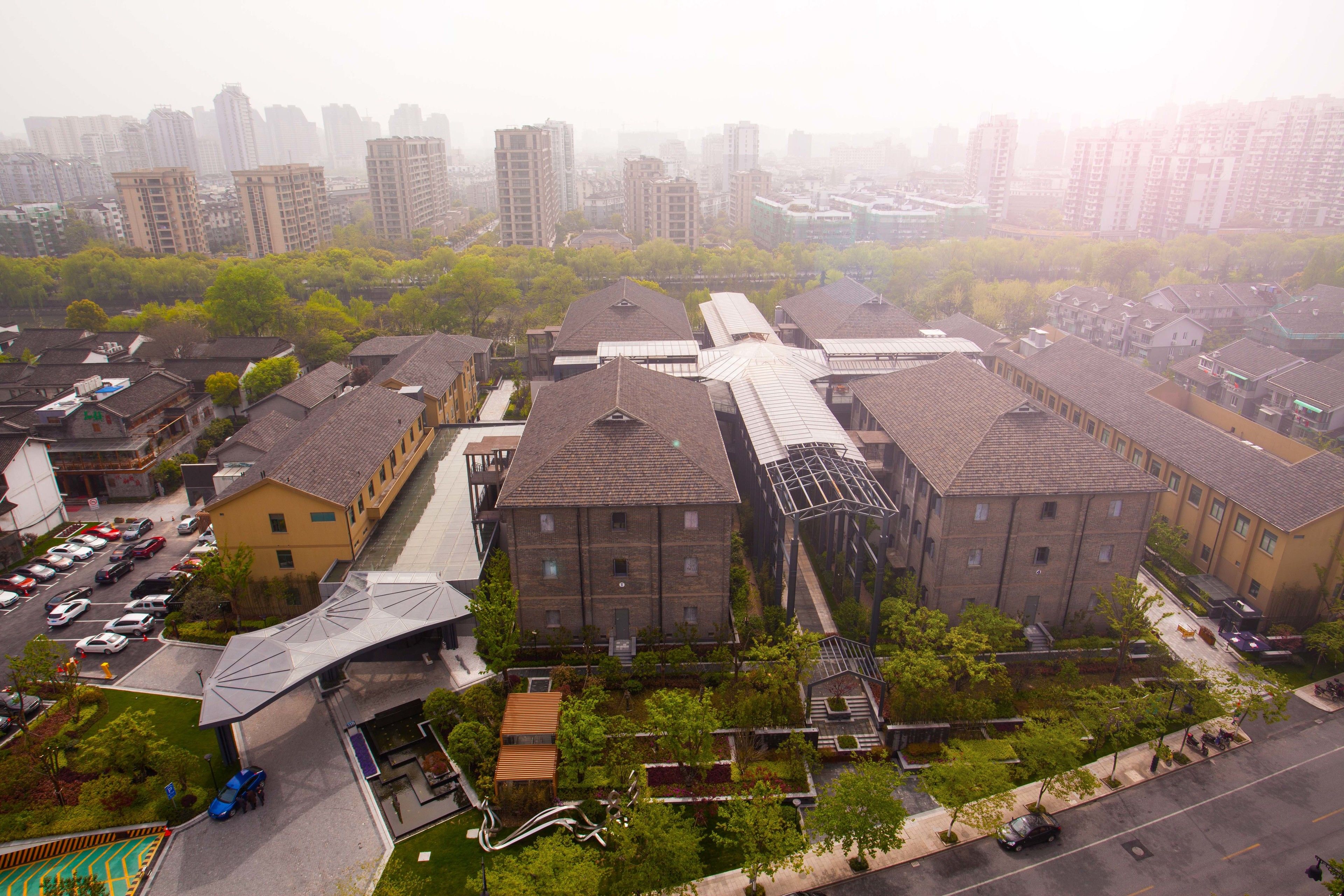 Una zona residencial con edificios modernos y tradicionales, un estacionamiento y un espacio verde con árboles.