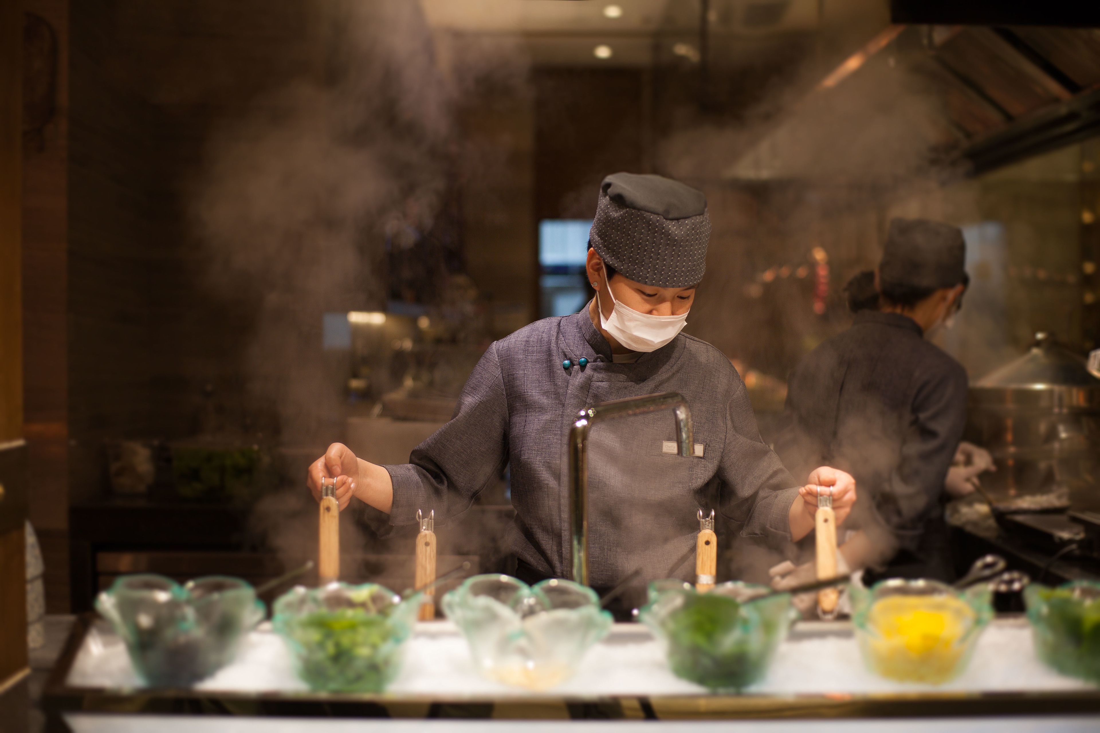 A chef preparing food in a kitchen with a stove and various cooking utensils.
