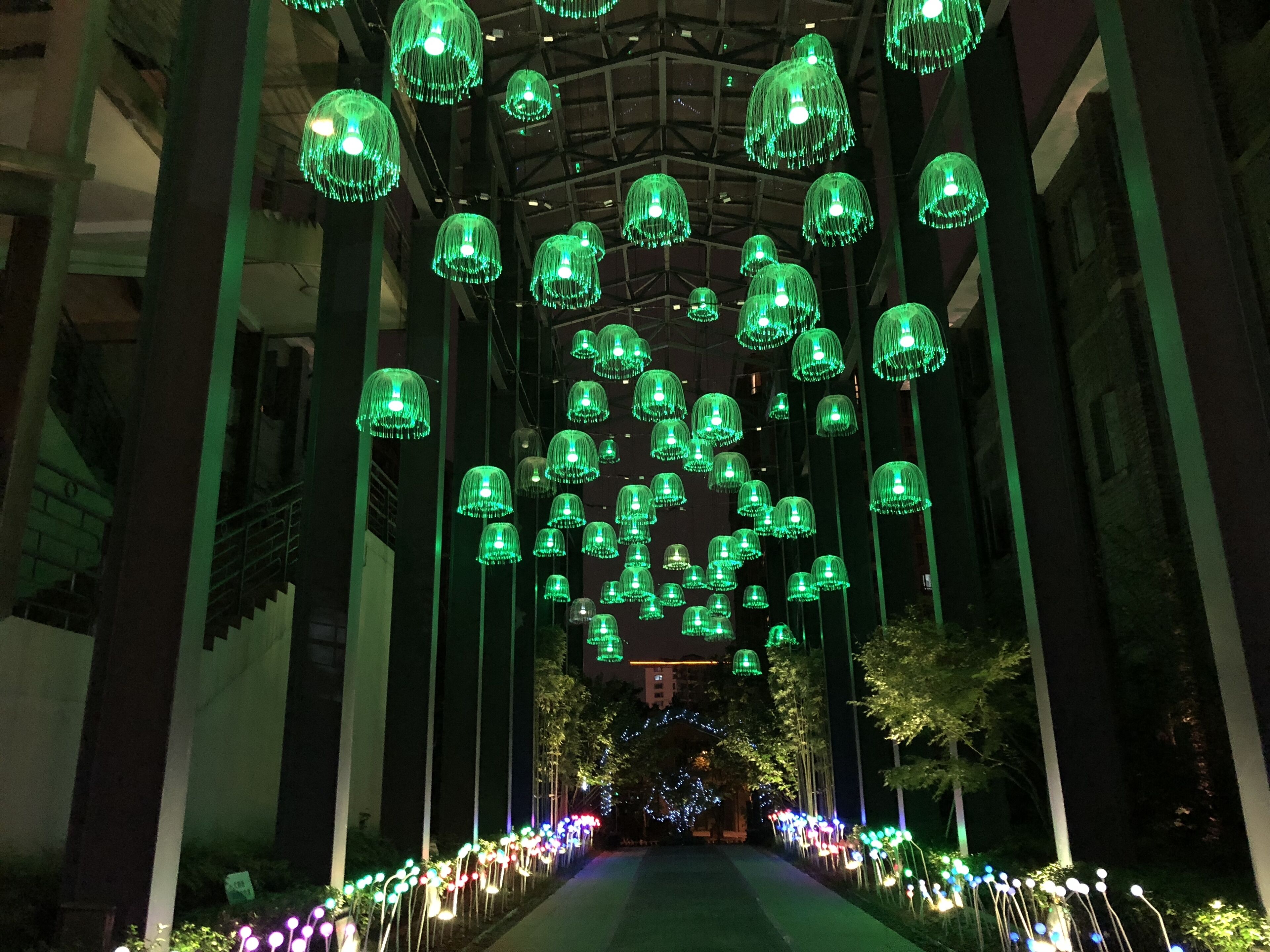 A corridor with hanging green lights and a pathway leading to a building entrance.