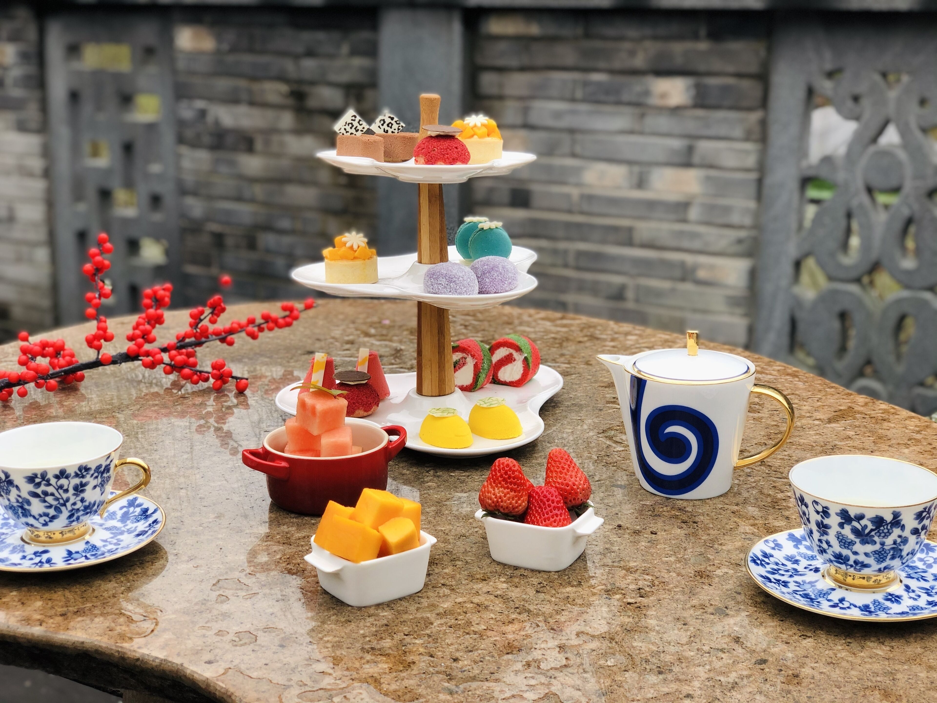 Un expositor escalonado para postres con diversos dulces coloridos, una tetera y dos tazas sobre una encimera de piedra.