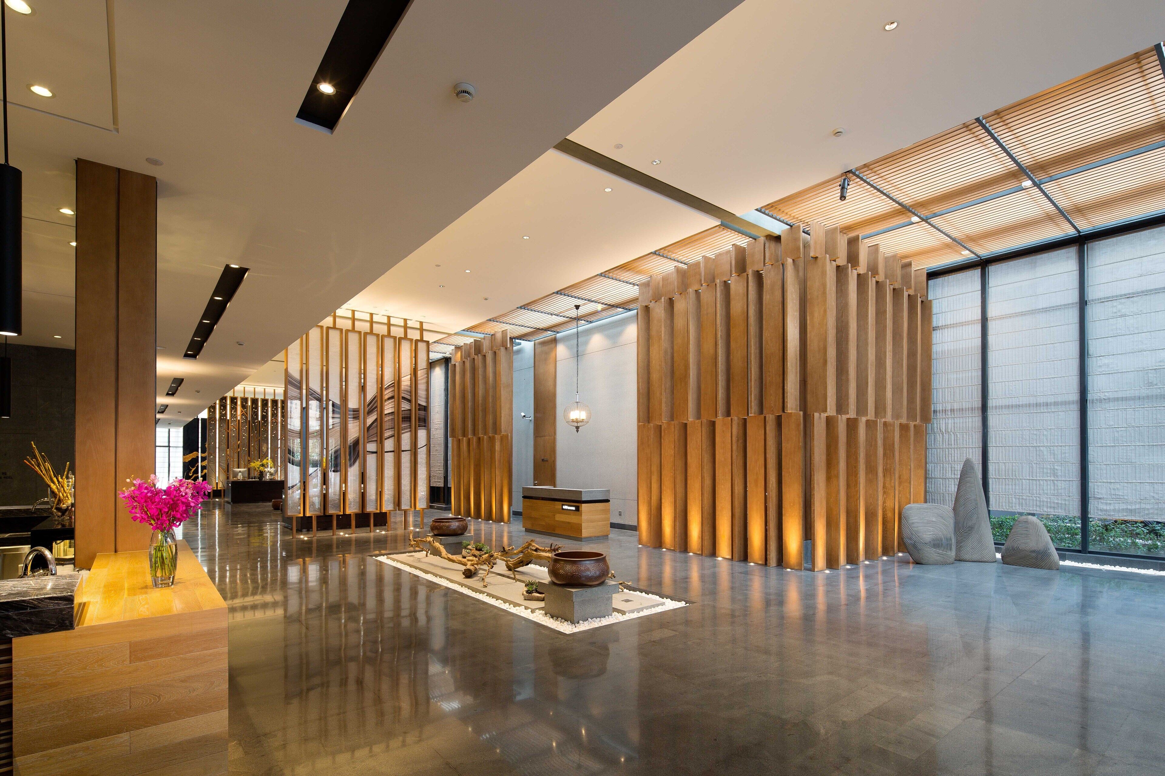 A spacious lobby with a modern design, featuring a reception desk, a wooden partition, and a large window providing natural light.