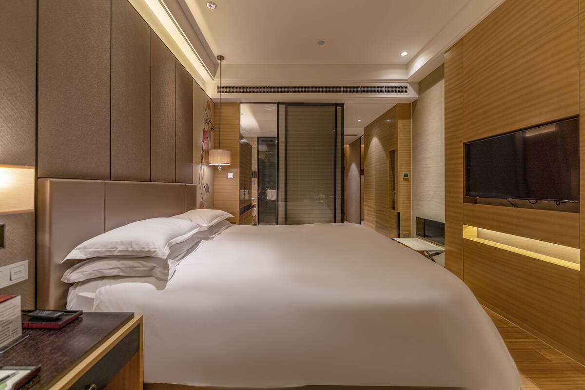 Een moderne hotelkamer met een groot bed, een bureau met een computer, een televisie en een schuifdeur naar een badkamer.