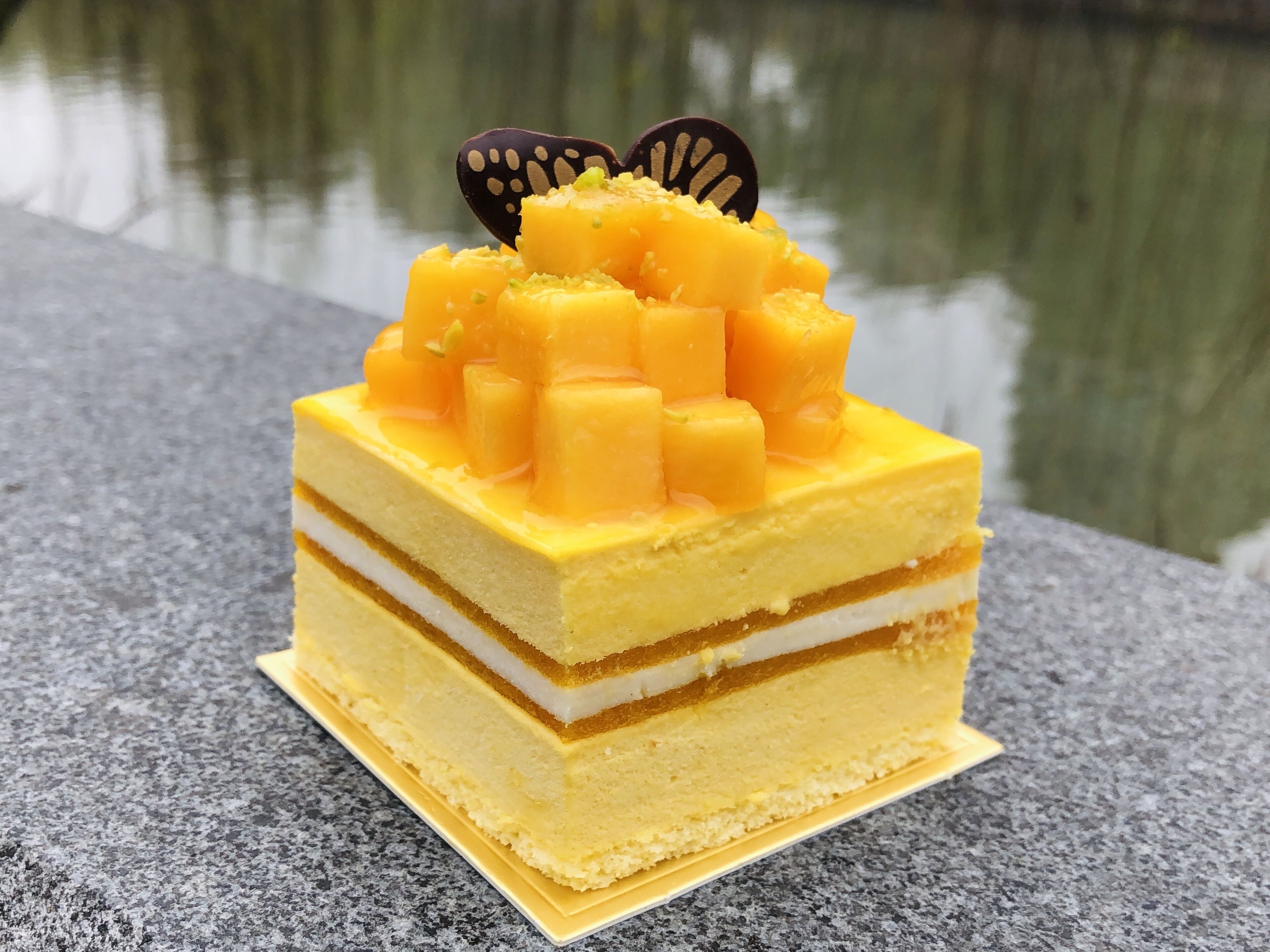 Un pastel amarillo en capas con trozos de mango encima, sobre una superficie de granito.