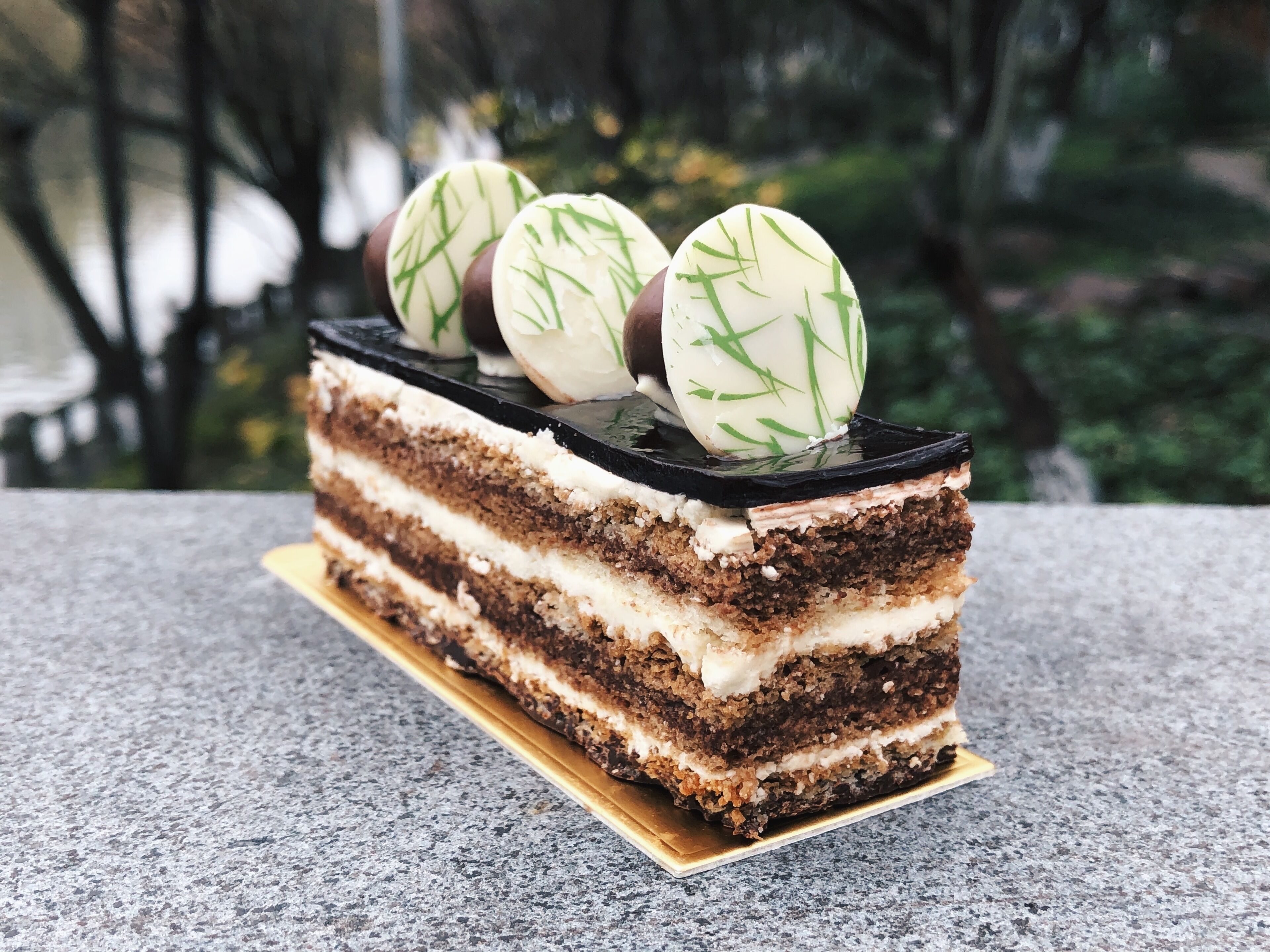 A slice of layered cake with white frosting and green decorations on top, placed on a wooden board.