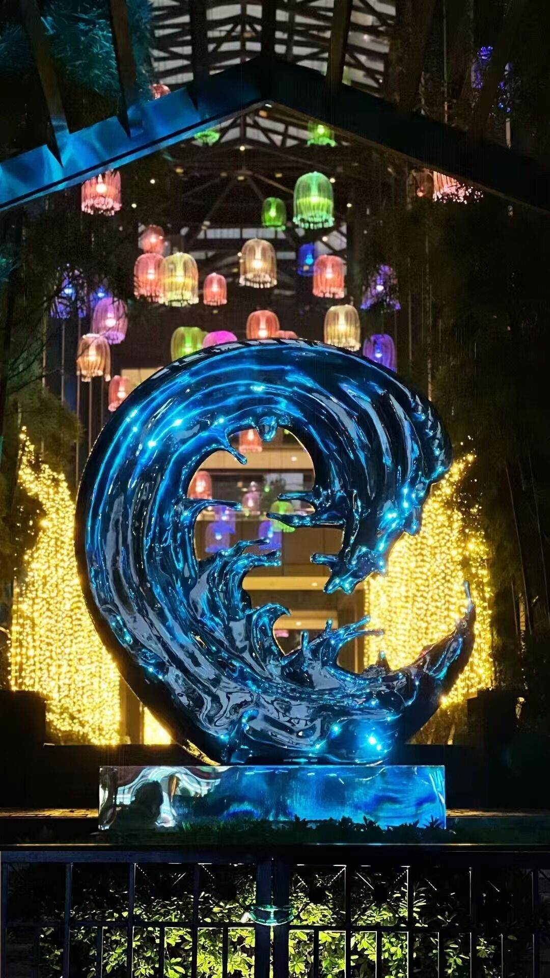 Una gran escultura de vidrio iluminada que evoca una forma de agua arremolinada, frente a un fondo de coloridas linternas colgantes.
