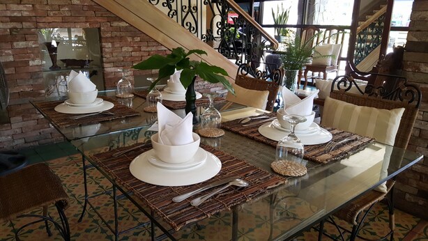 A dining table set with white plates, bowls, and silverware, surrounded by wicker chairs and a glass table. - Roxas President's Inn (Roxas City)