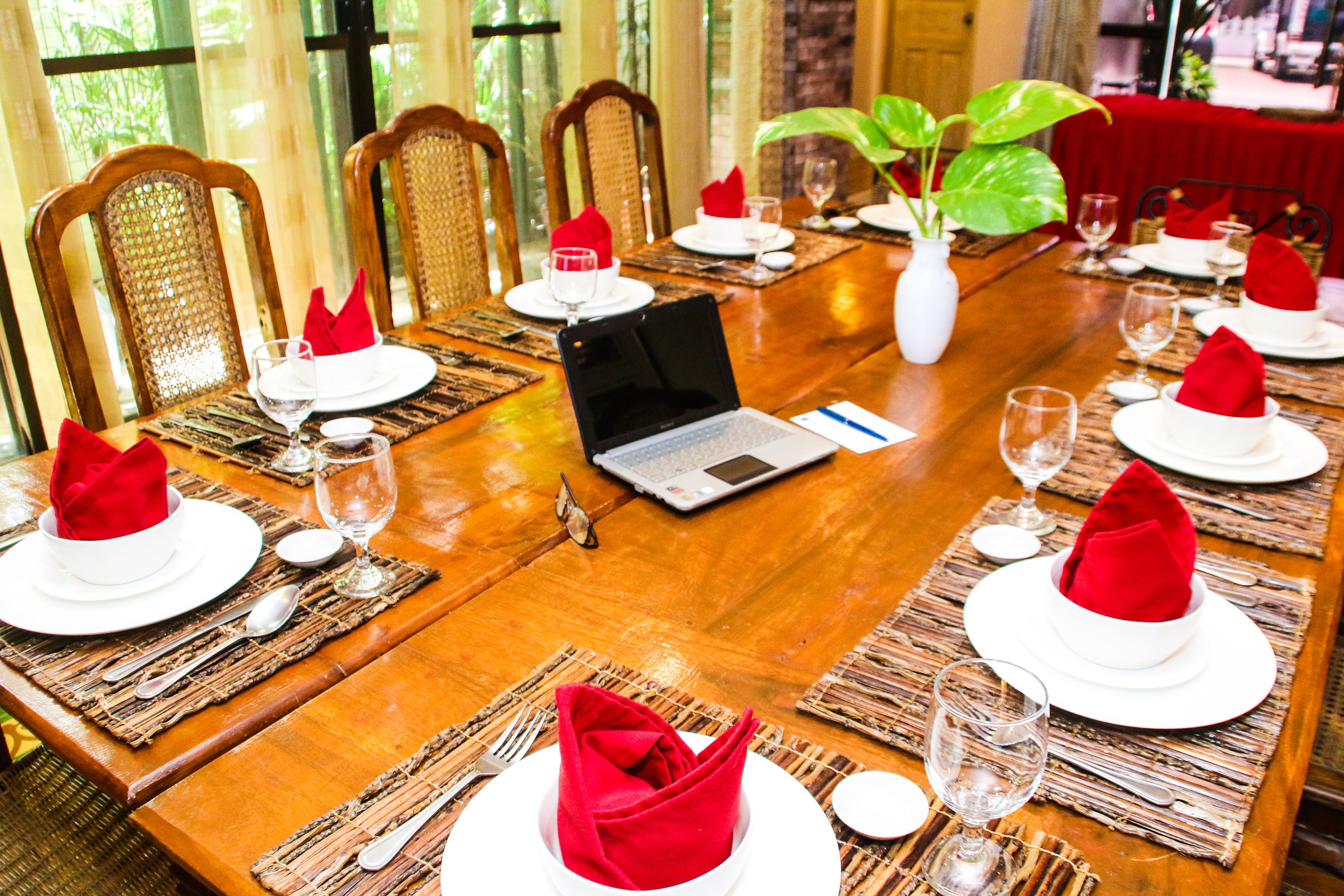 A dining table set with white plates, red napkins, and wine glasses, with a laptop on the table.