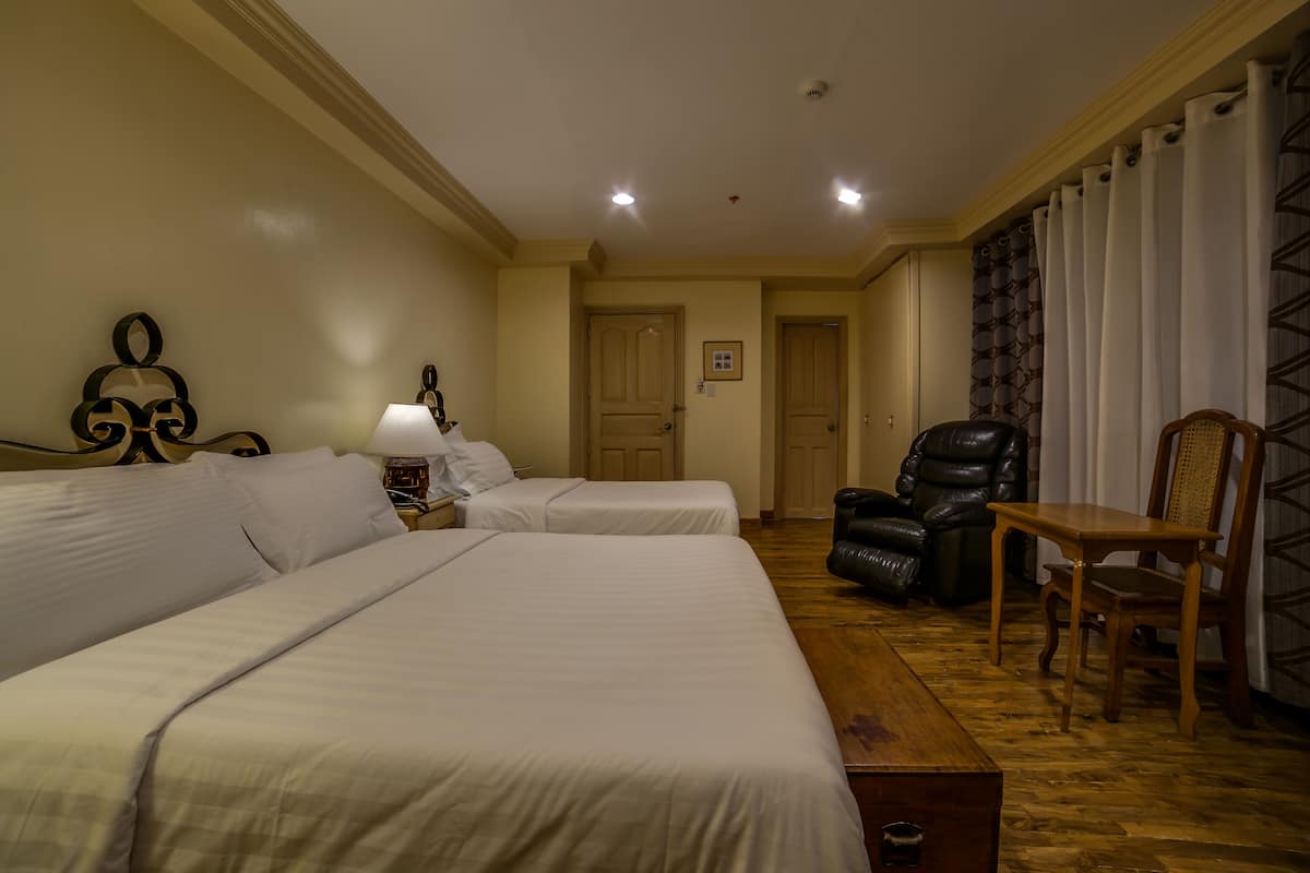 Een hotelkamer met twee bedden, een houten tafel, een lederen stoel en een deur naar een andere kamer.