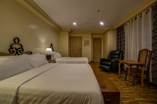 Une chambre d’hôtel avec deux lits, une table en bois, un fauteuil en cuir et une porte donnant sur une autre pièce.