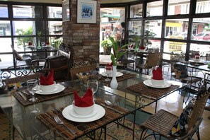 Un restaurant dont les tables sont dressées pour le service, avec des plateaux en verre et des chaises en osier.