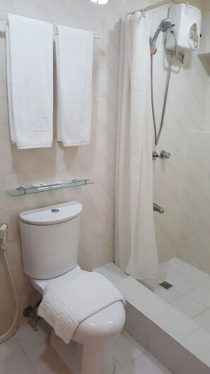 Une salle de bain équipée de toilettes, d’une  étagère en verre, d’une douche et de deux serviettes accrochées au mur.