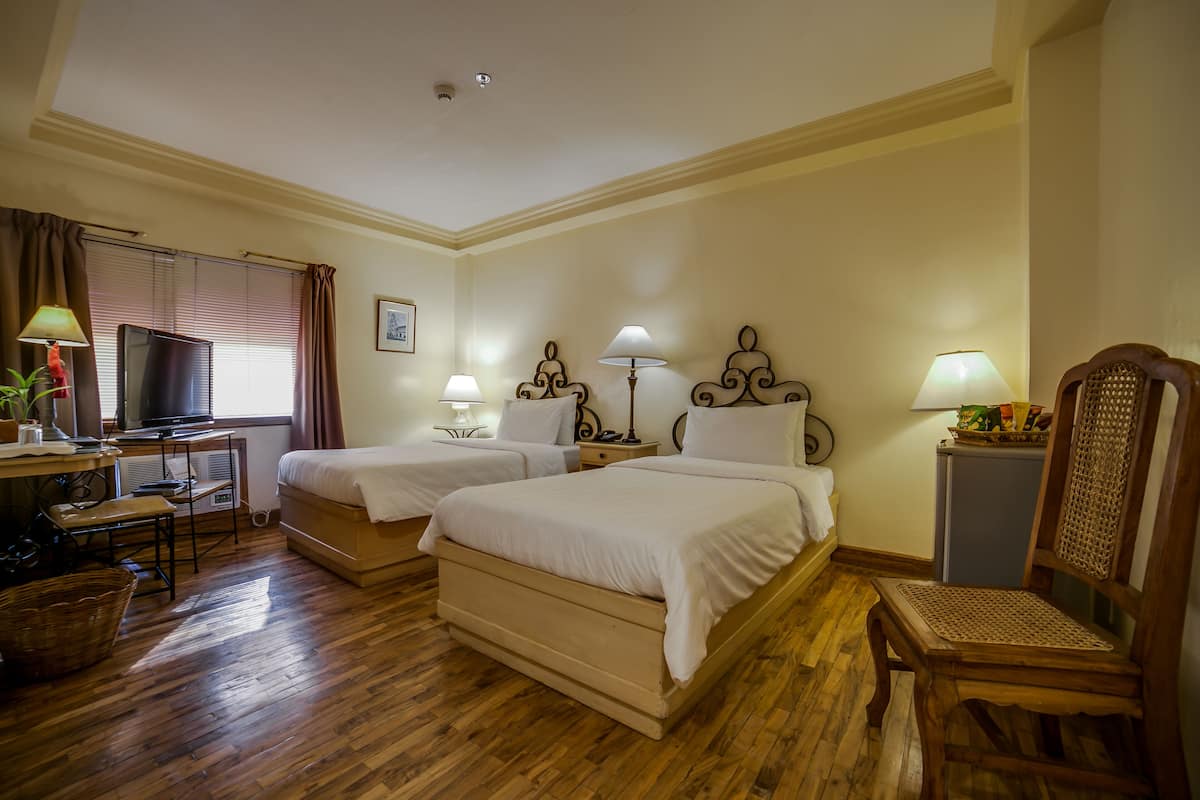 Een hotelkamer met twee bedden, een bureau met een computer, een stoel en een klein kastje.