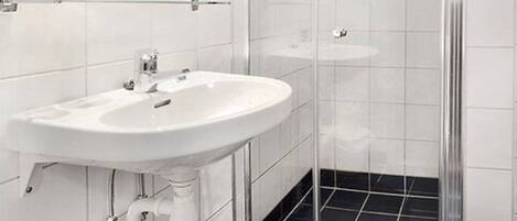 A modern bathroom with a white sink, a glass shower enclosure, and black-tiled flooring.